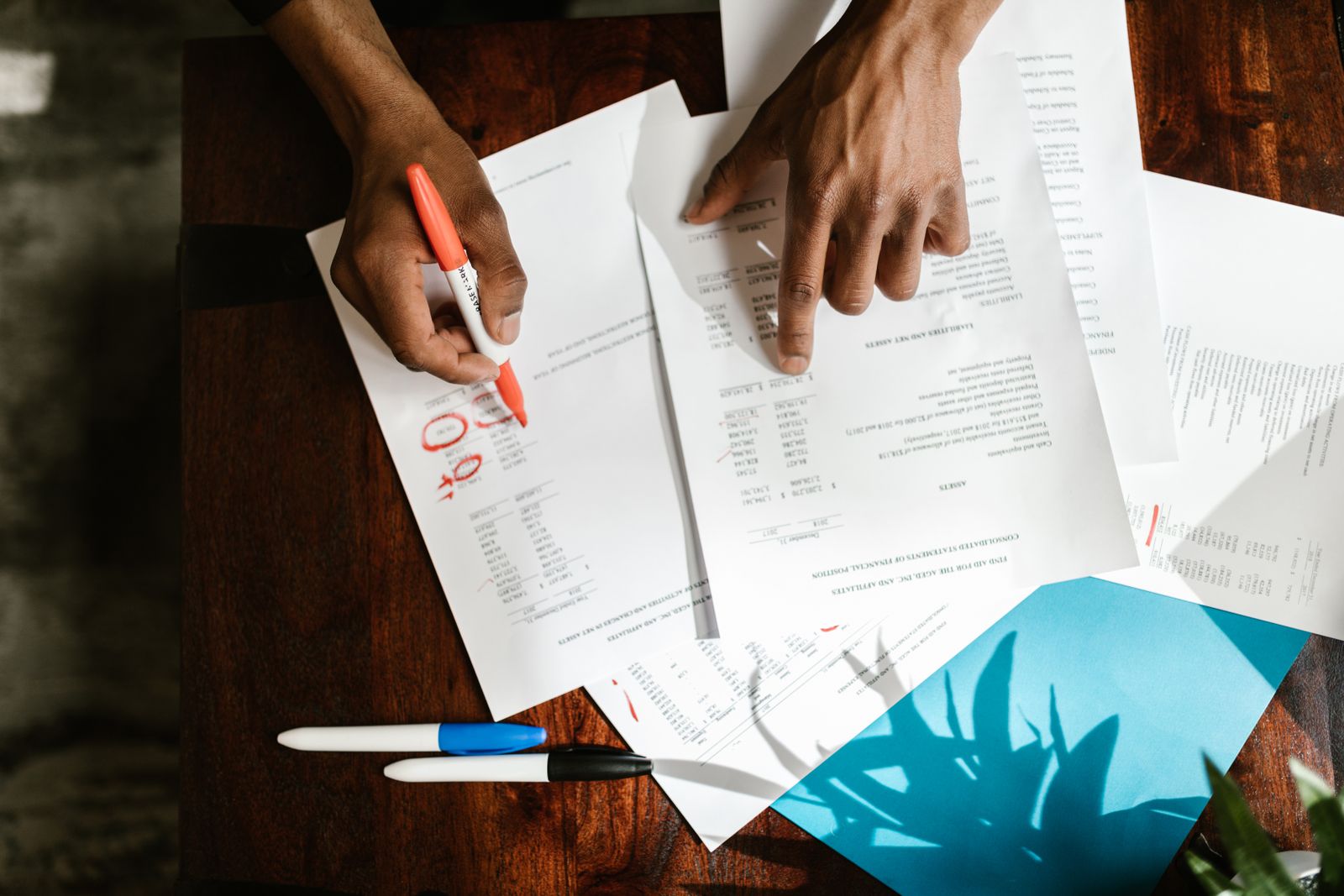 Hands going over printed financial statements, circling figures with a red marker.