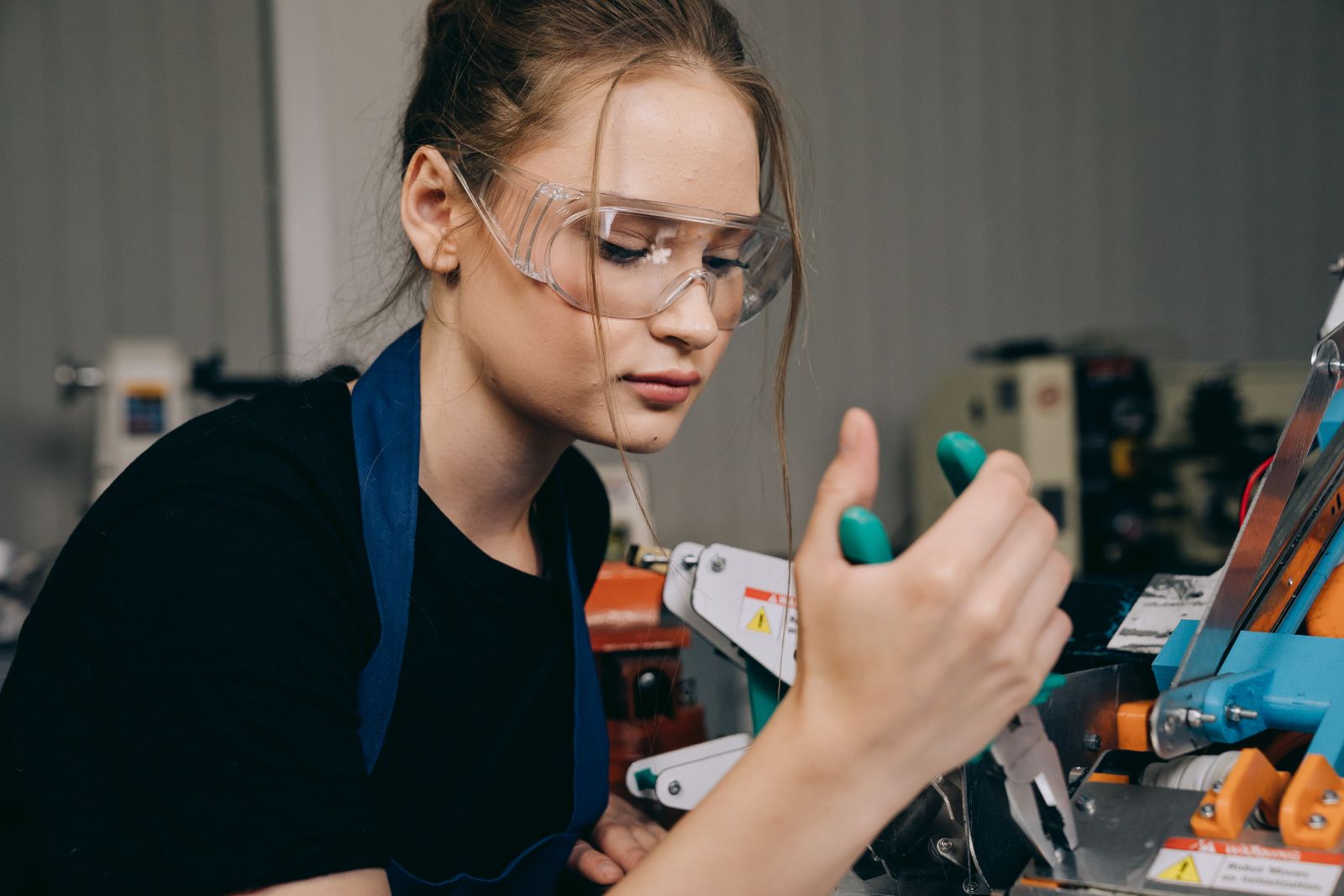 A trainee in safety goggles concentrating on a machine at a workshop bench.